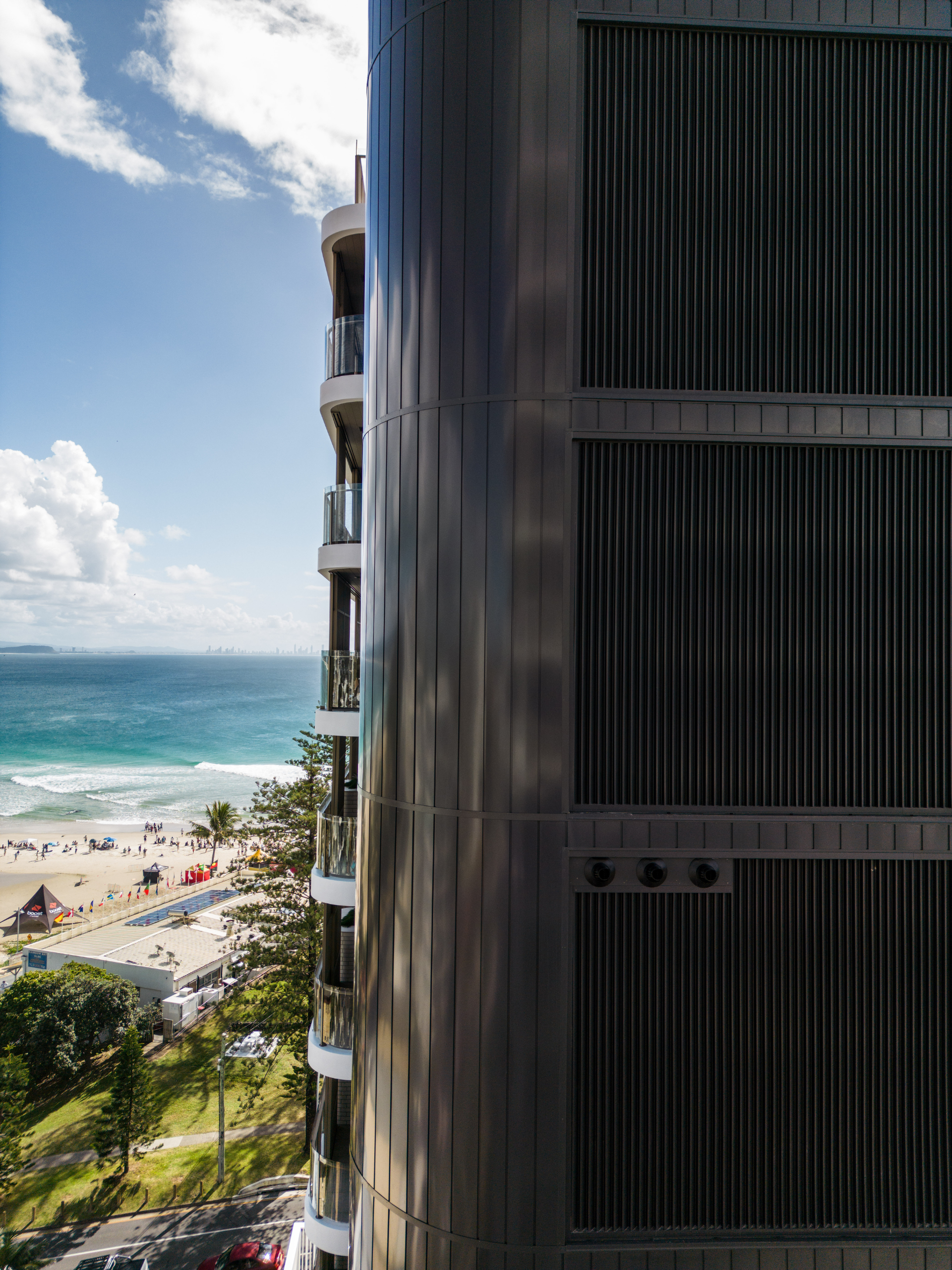 High rise apartment building, showcasing a weatherboard look façade in black with the QLD coast in the background