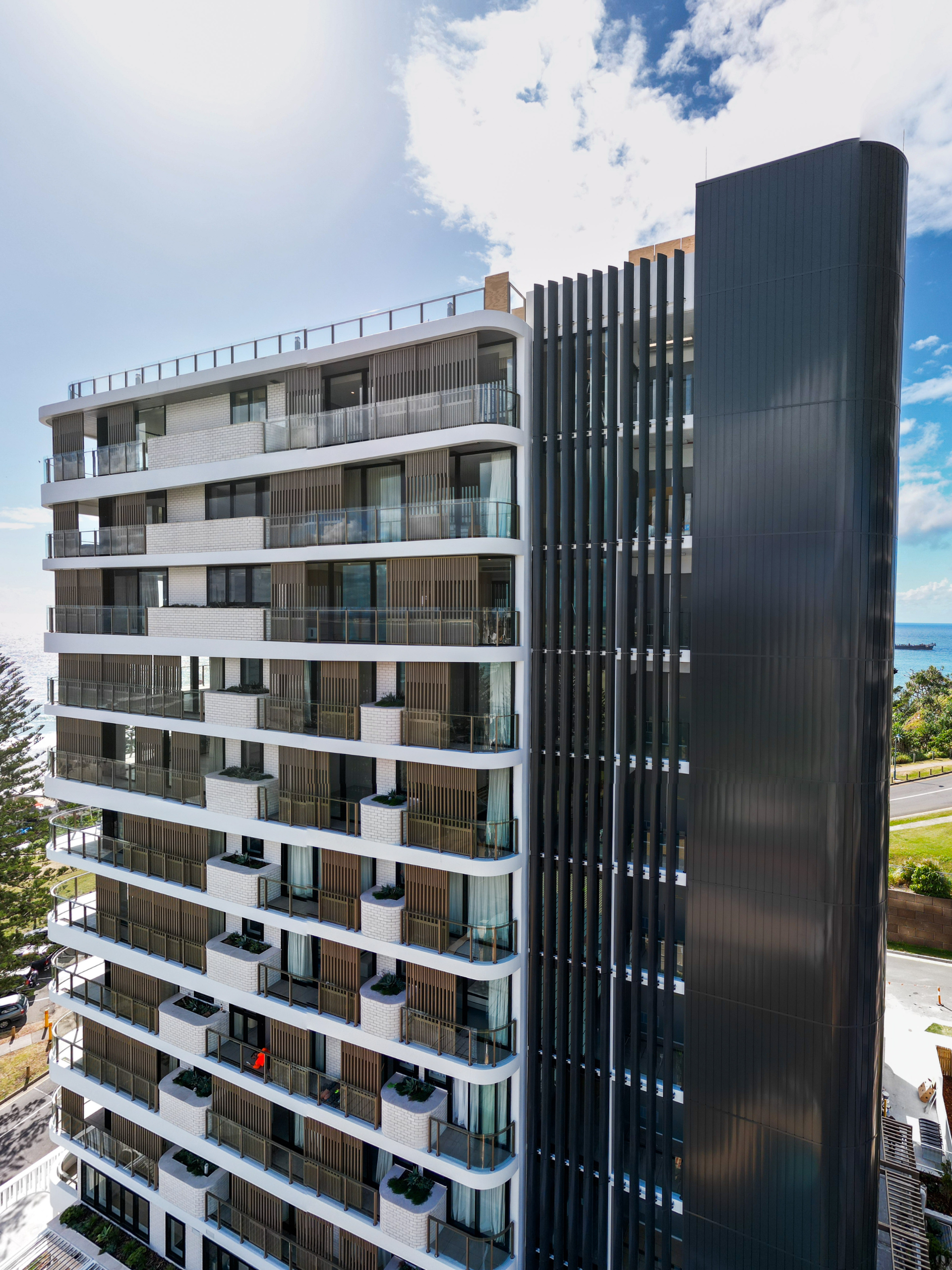 High rise apartment building, showcasing a weatherboard look façade in black with the QLD coast in the background