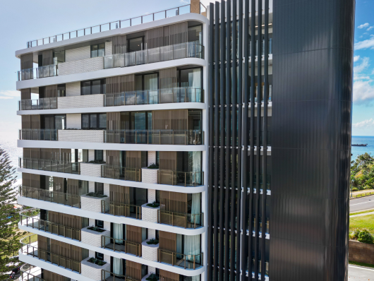 High rise apartment building, showcasing a weatherboard look façade in black with the QLD coast in the background